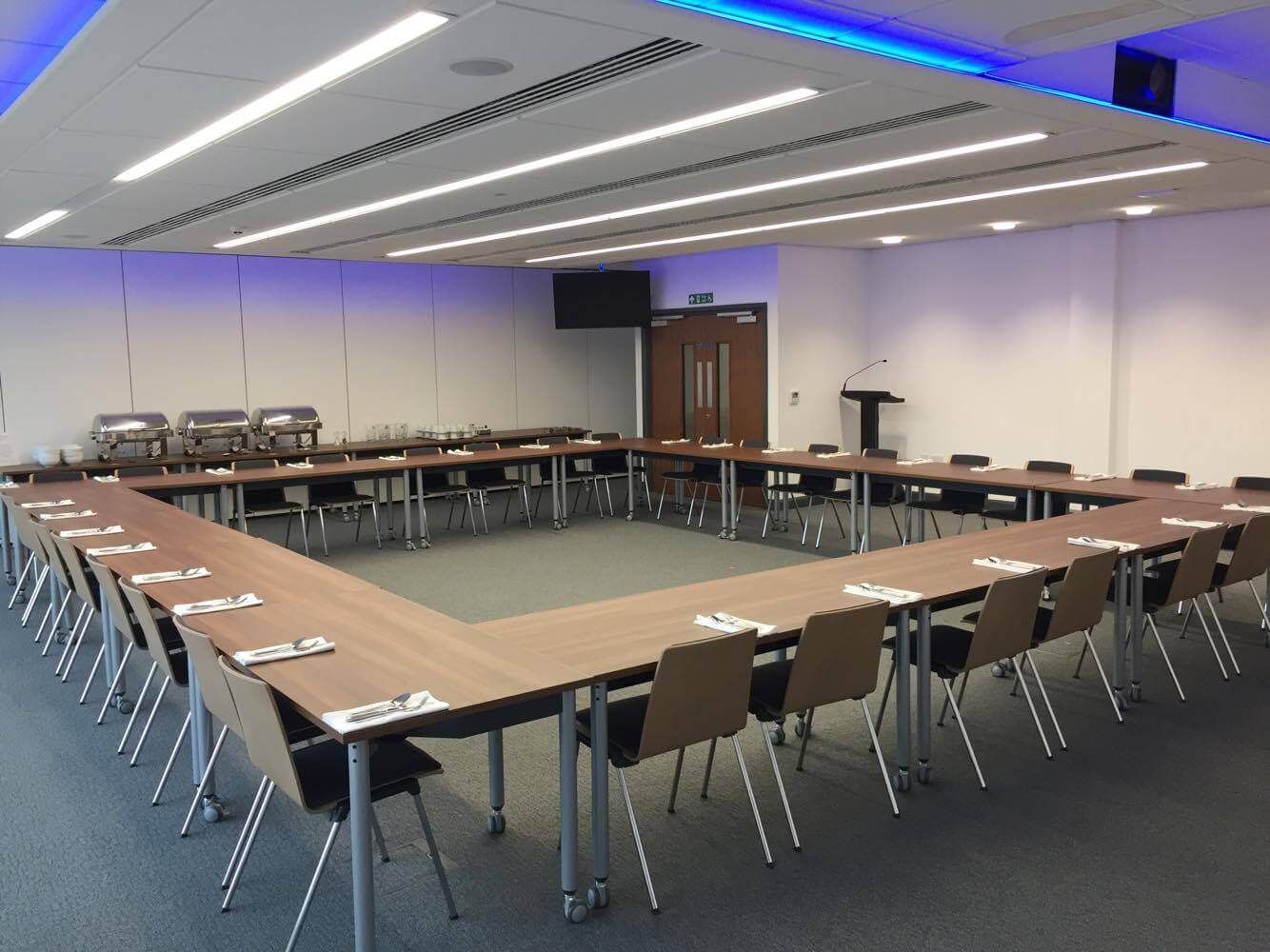 A single row of tables and chairs arranged in a square in a large meeting room