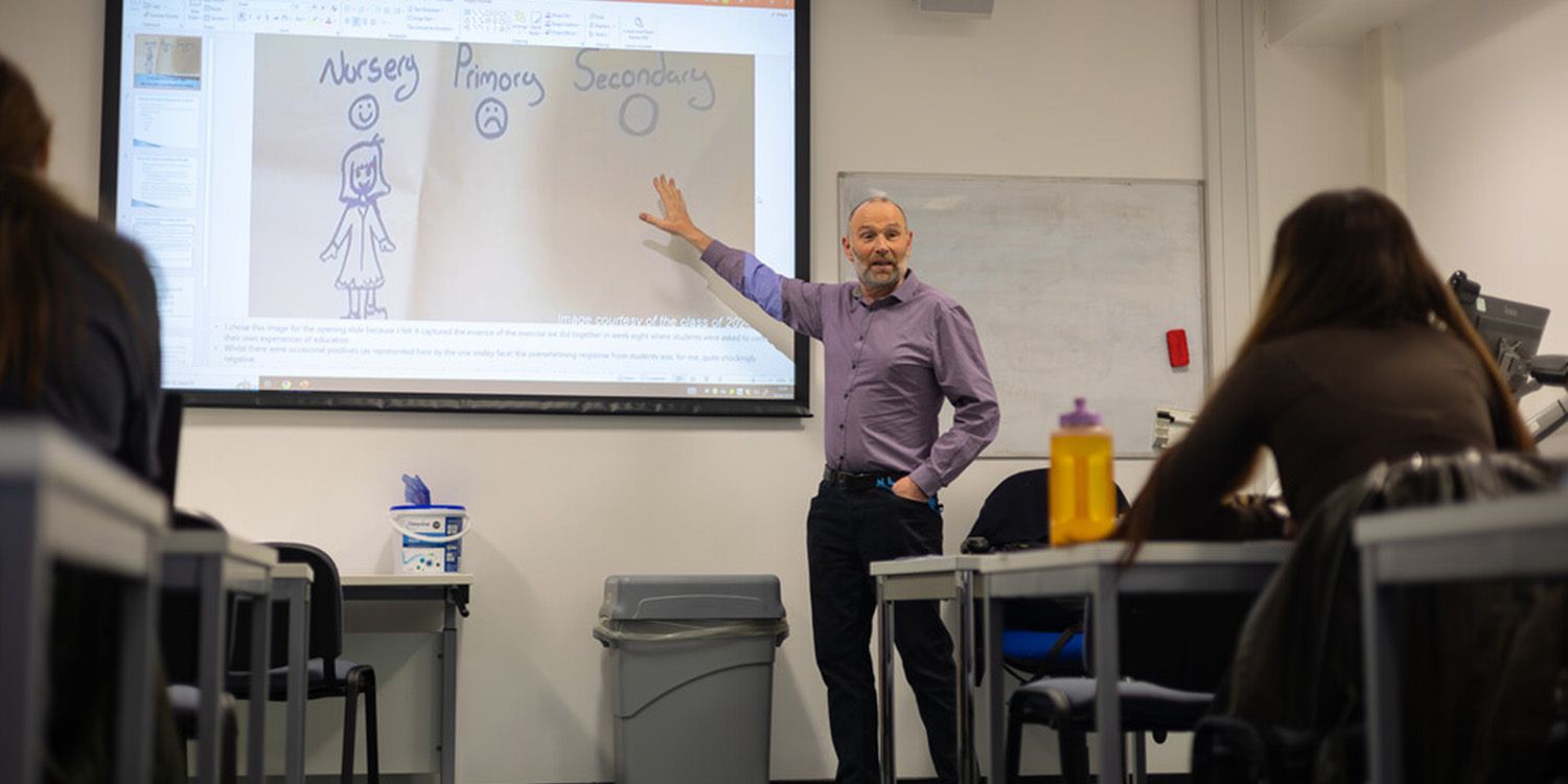 An academic teaching a class, pointing to a large screen