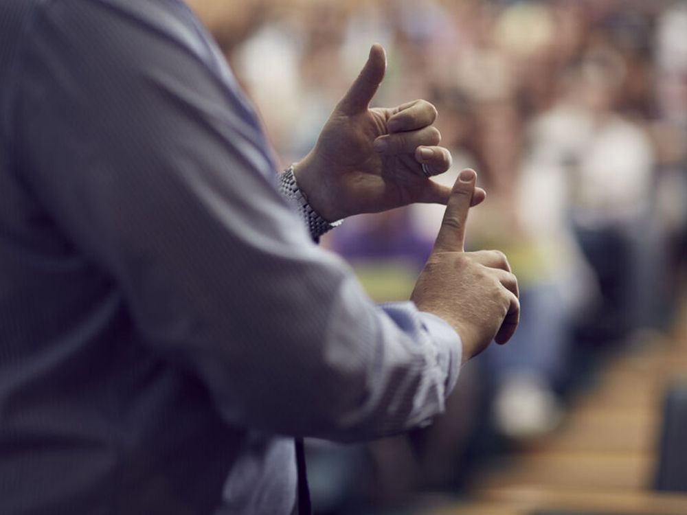 A lecturer's hands in the foreground of a full lecture theatre of students