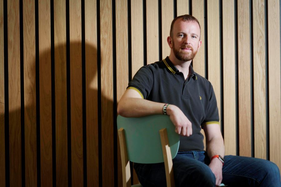 Drew Dalton sitting on chair in front of wooden slated wall