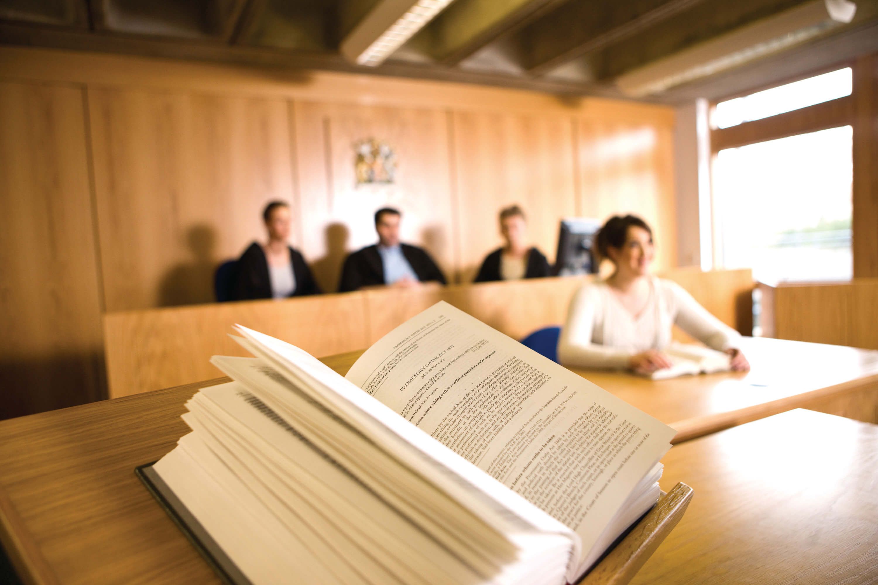 Four Law students sitting in the mock law court out of focus, with an open book in focus in the foreground