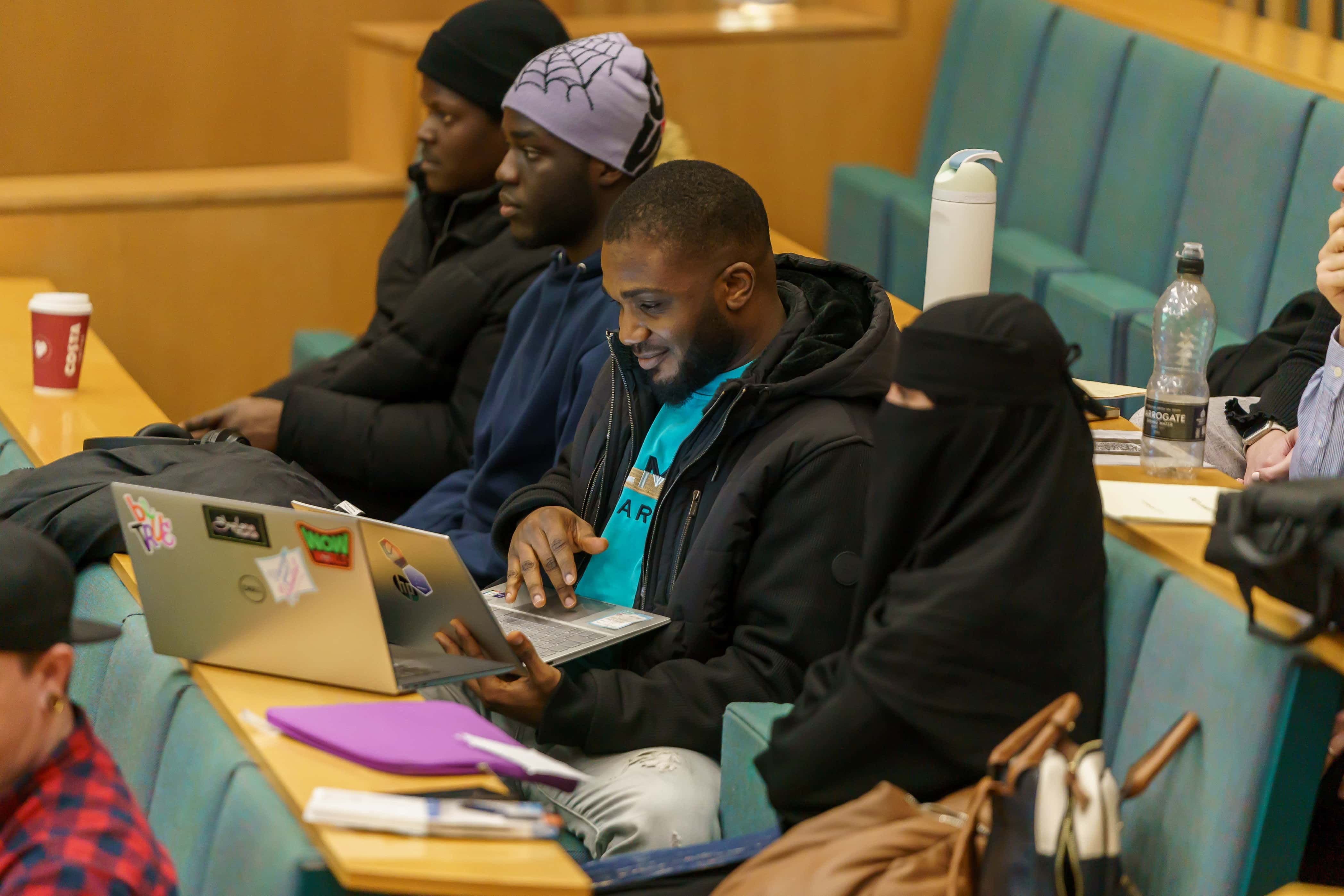 A group of computer science students sitting together in a lecture theatre, working on the Hackthon on their laptops