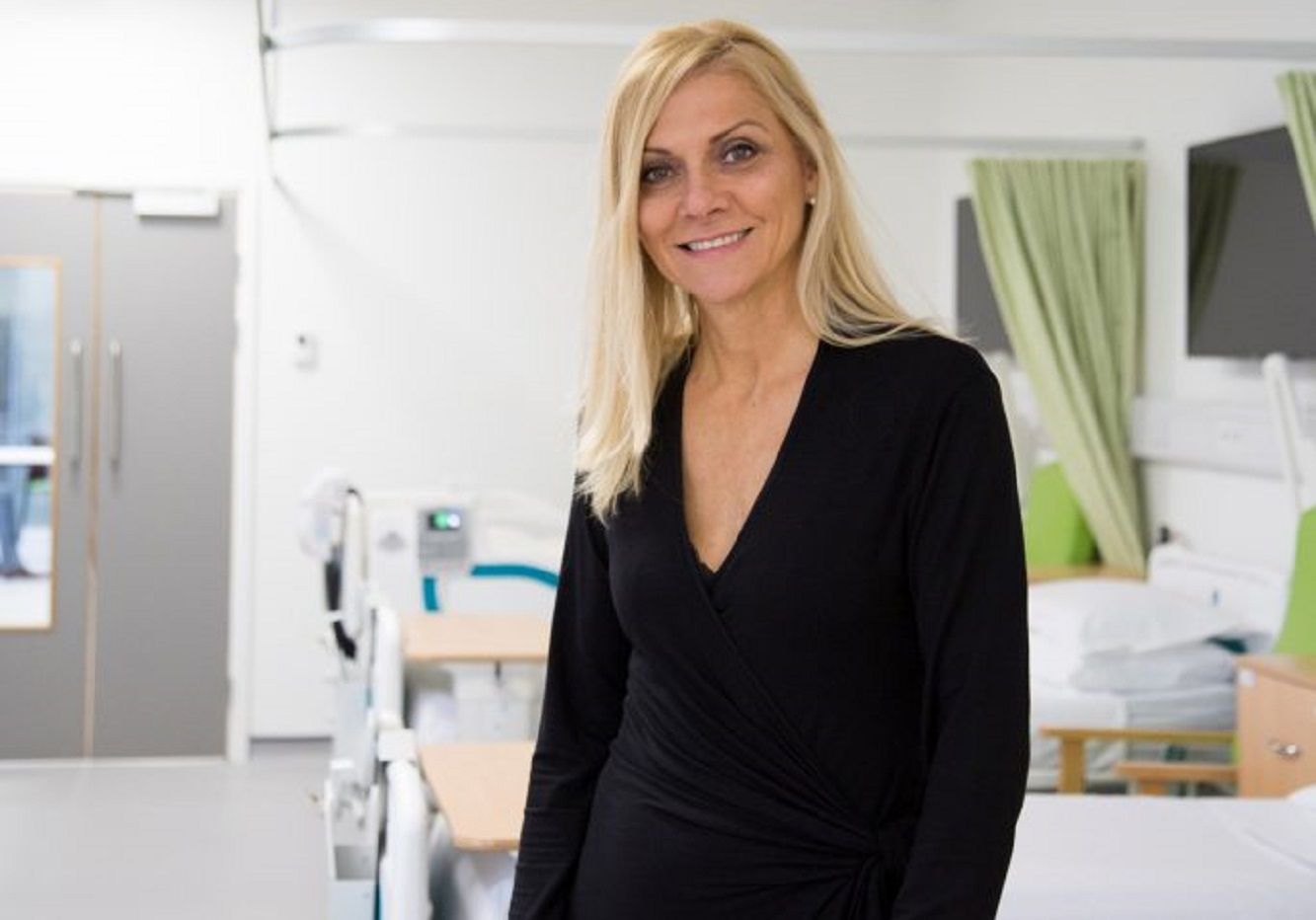 Professor Yitka Graham standing in a mock hospital ward smiling to camera