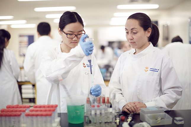 A student using a pipette in a pharmaceuticals lab while another student stands and watches