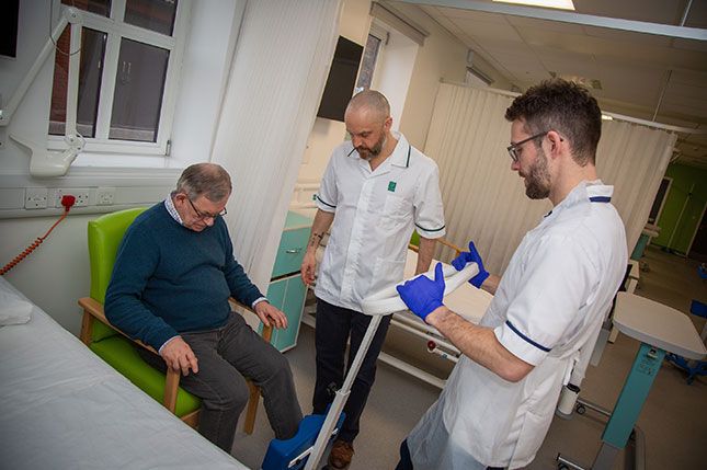 A physiotherapist and an occupational therapist helping a patient to stand in a hospital ward