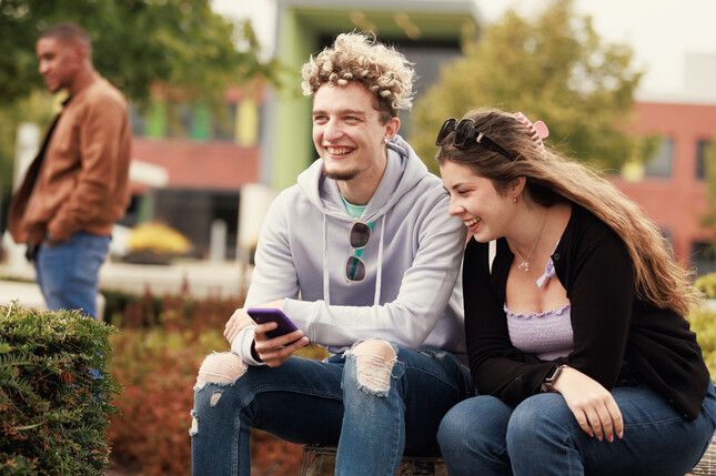 Two students laughing outside whilst looking at a phone