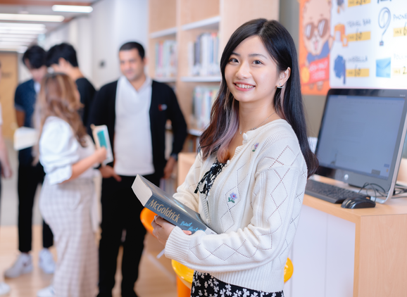 A student smiling at the camera with a book in their hand