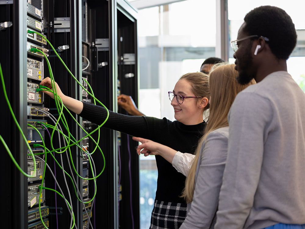 A group of computer science students plugging cables into a server rack