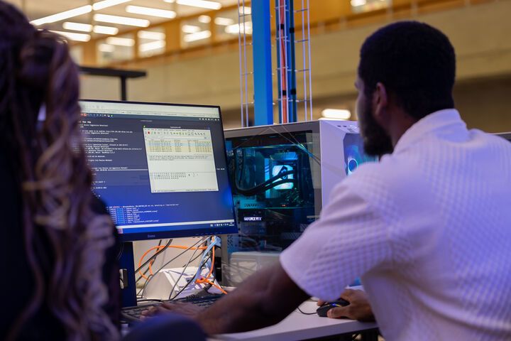 Two computer science students sitting at a computer, looking at something that is on the monitor
