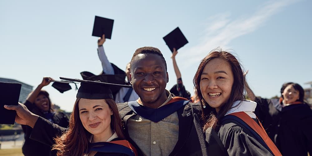 Graduates smiling at the camera and throwing caps in air