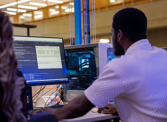 Two computer science students sitting at a computer, looking at something that is on the monitor