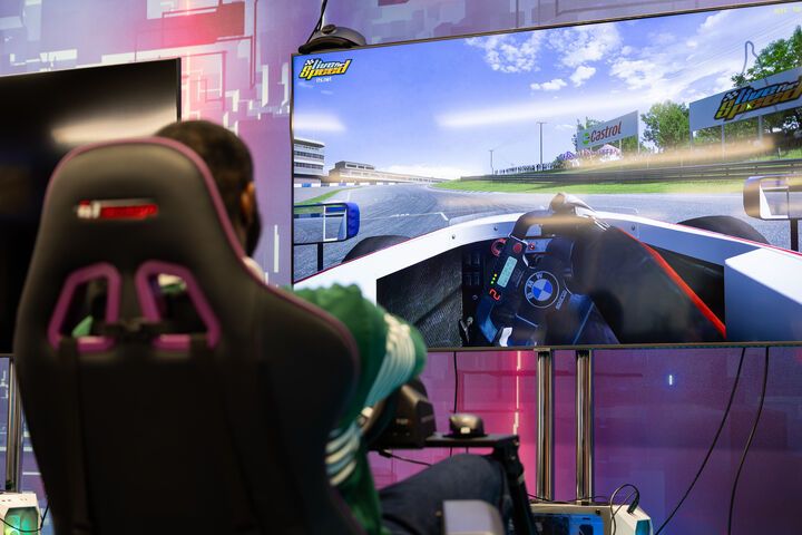 A Game Development student sitting in a gaming chair playing a racing game in a sim racing rig