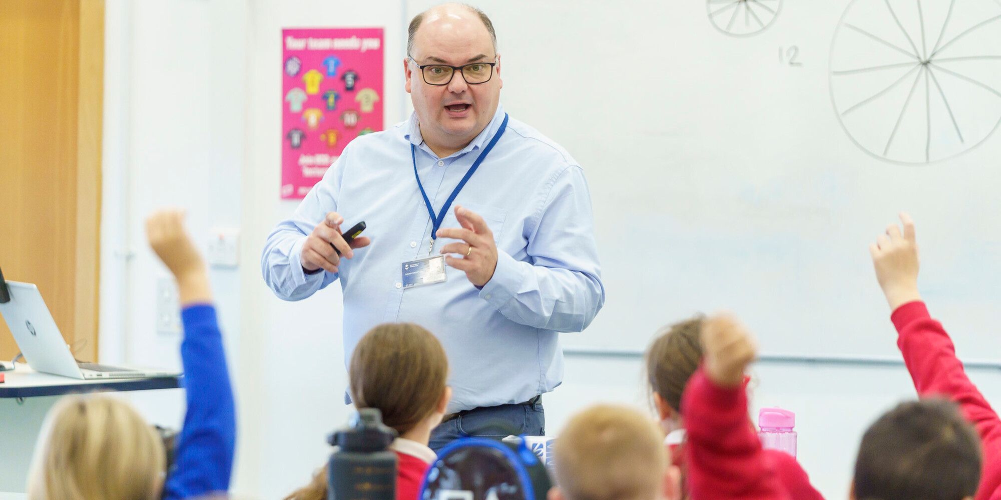 An academic speaking to a group of children who have their hands in the air