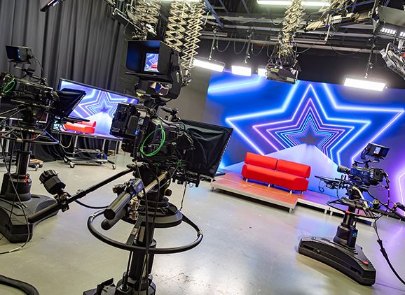 Film cameras in a TV studio pointing at a set with a sofa