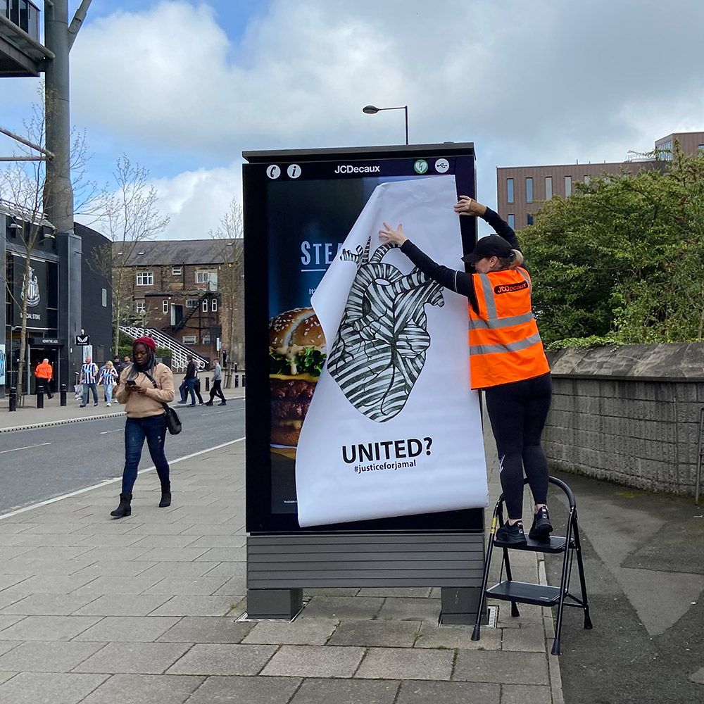 A student hanging art up on the side of a bus stop