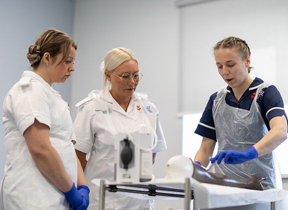 Three nursing students working with a manikin arm