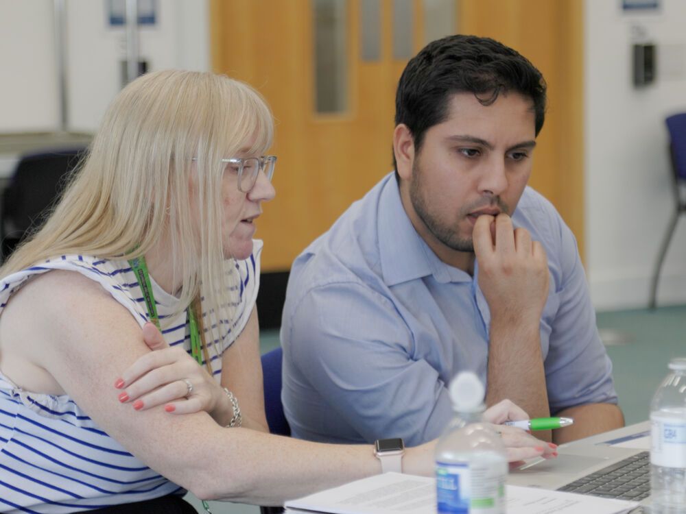 A lecturer sitting with a student at a laptop, looking at something on the screen together