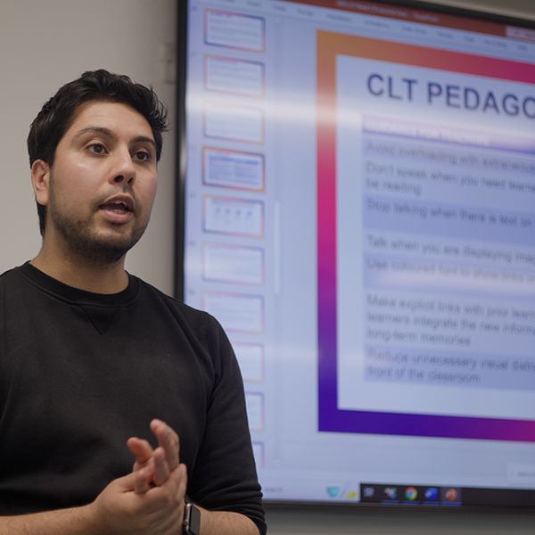 A lecturer teaching with a screen behind him