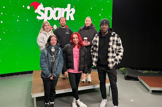 Six students facing the camera and smiling, standing in front of a television screen that has the Spark Sunderland logo on it