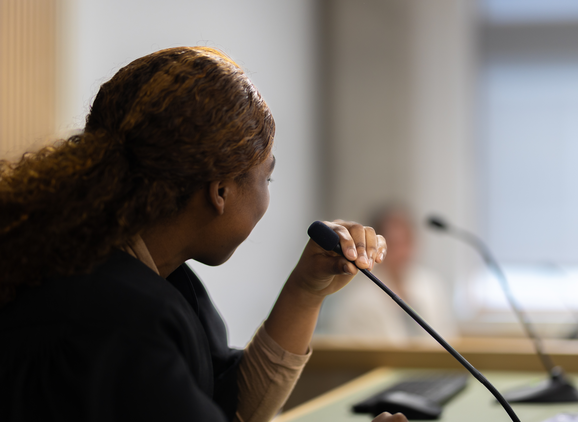 A student in a black law robe in a mock court talking into a microphone