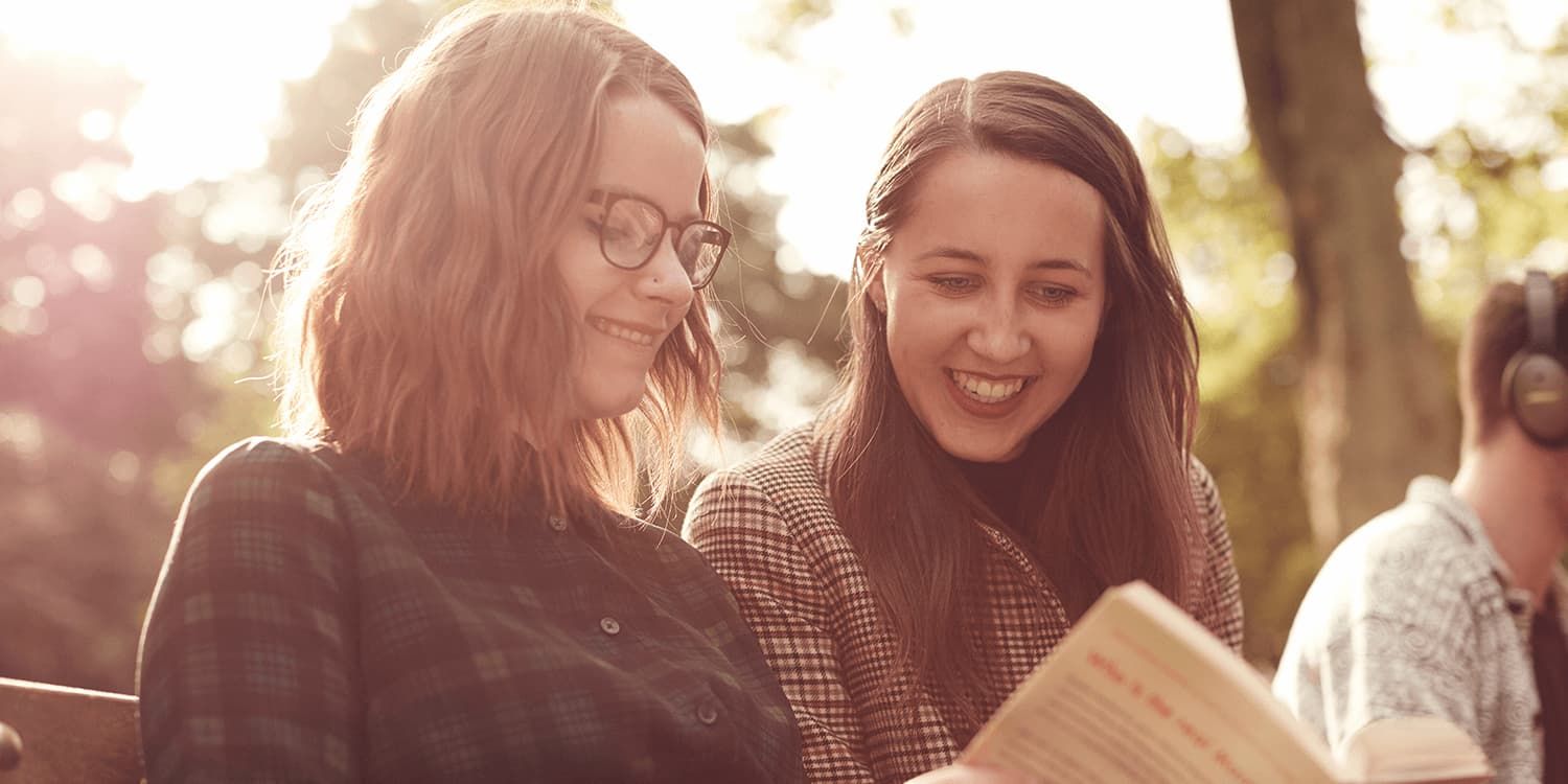Two students smiling whilst reading a book together