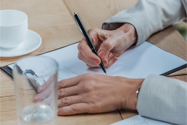 A hand holding a pen and the other hand leaning on a clipboard writing