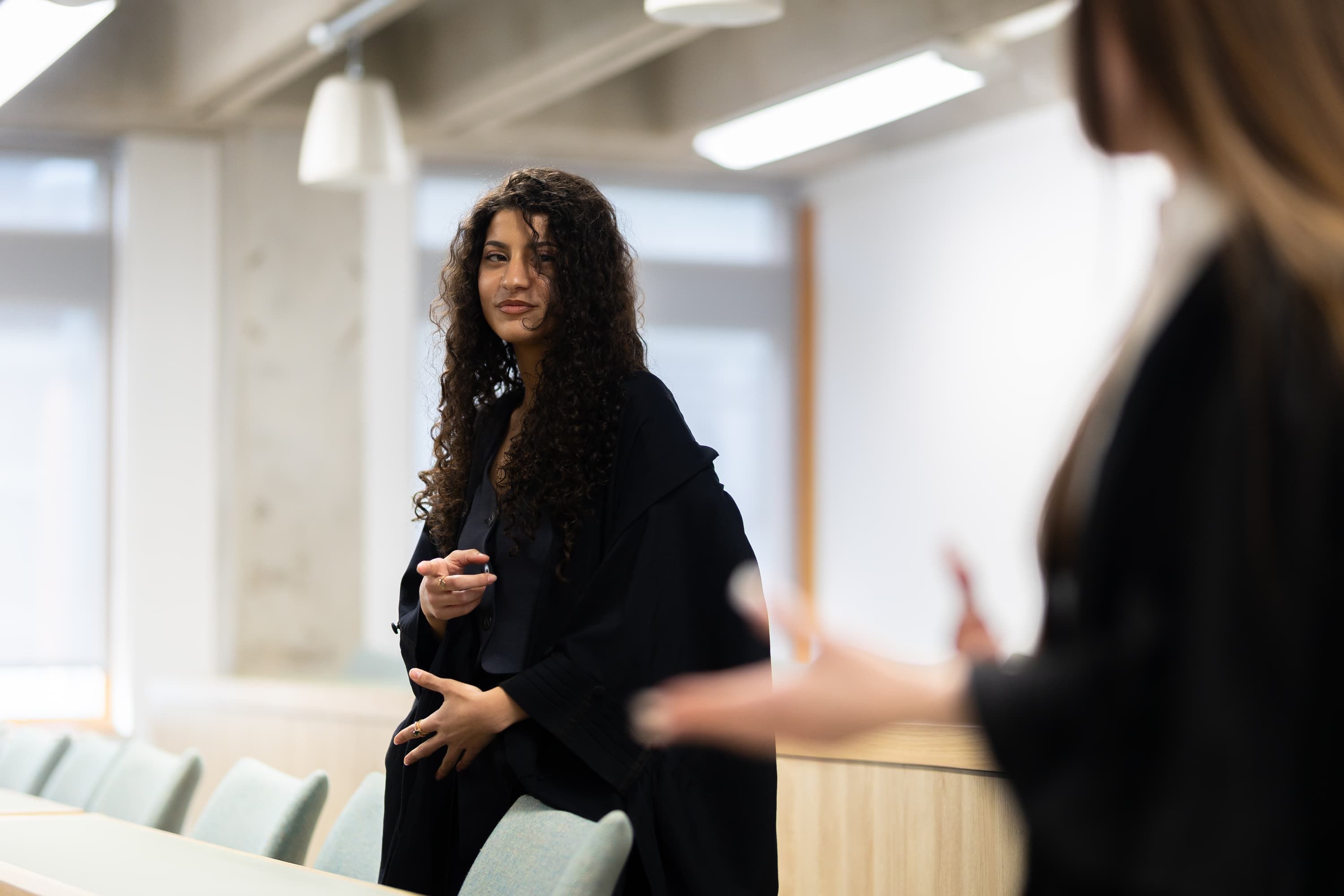 A law student in a black robe standing at the front of the mock court engaging in conversation