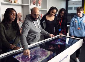 A medical educator and four students stand at the anatomage table during a practical session. The educator is showing the students the different parts of the heart.