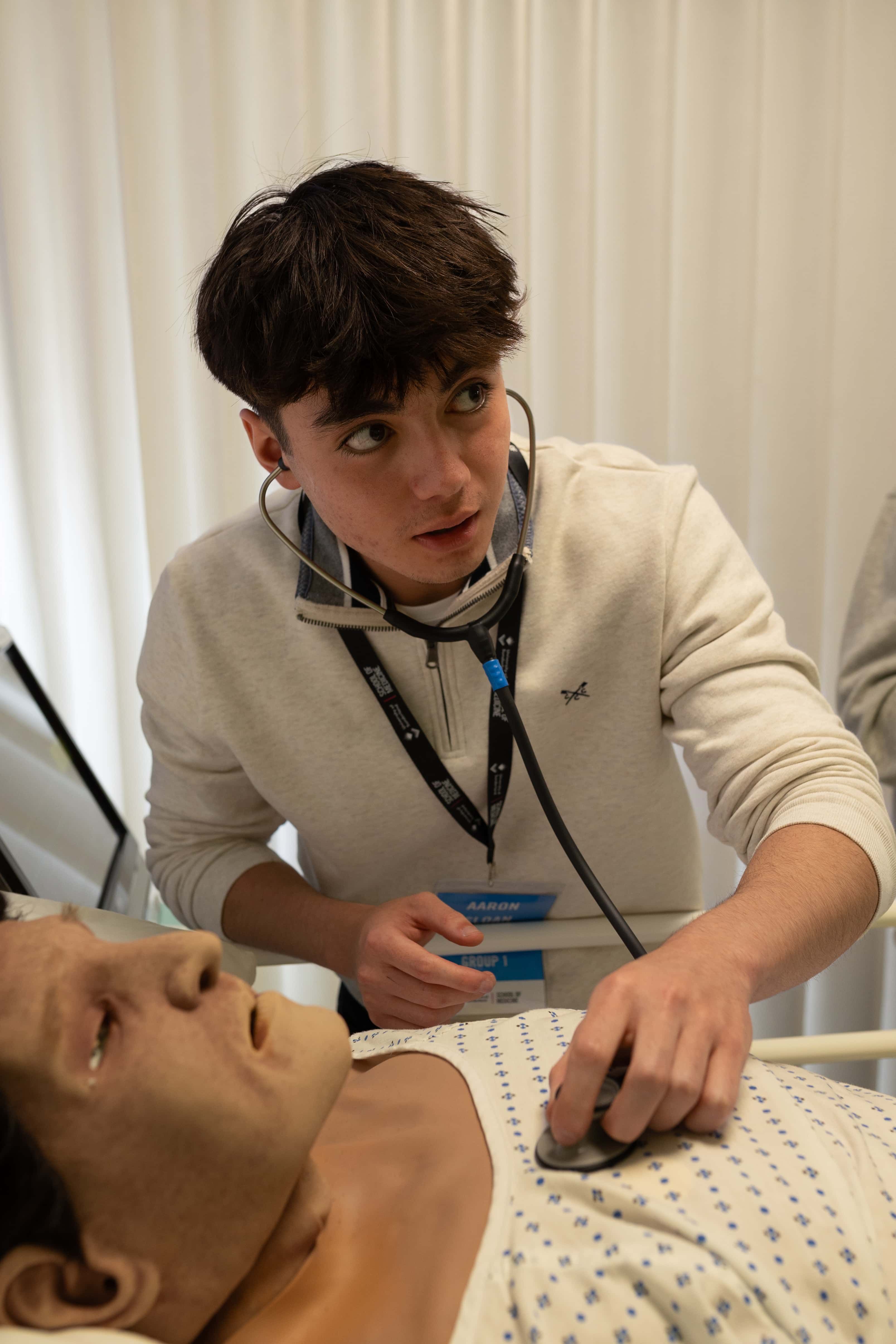 A medstart student using a stethoscope on a Manikin during a simulation