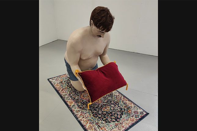 A sculpture of a man kneeling down on a rug, holding a cushion