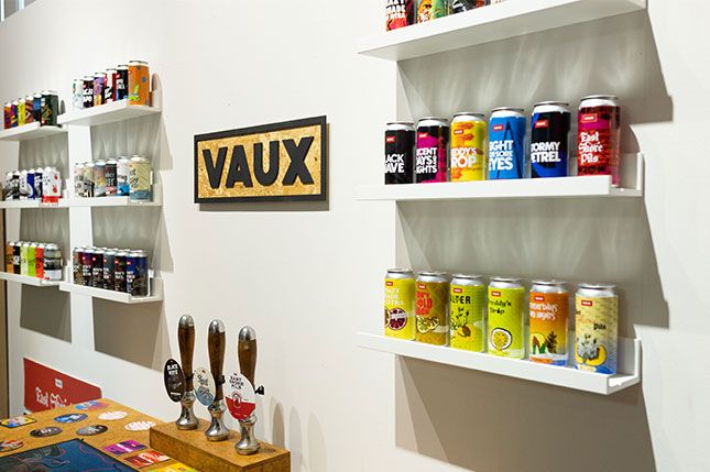 Colourful cans of lager on a shelf next to three pumps and a sign that says Vaux