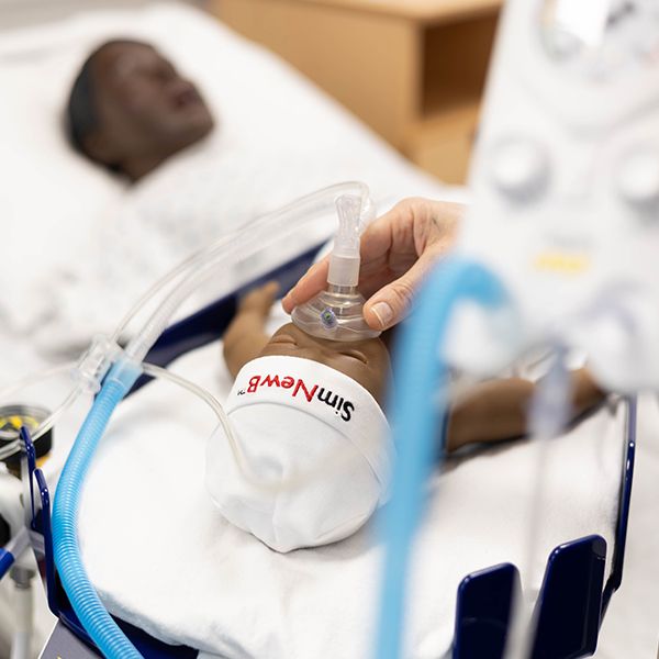 A students hand putting an oxygen mask on a SIM baby