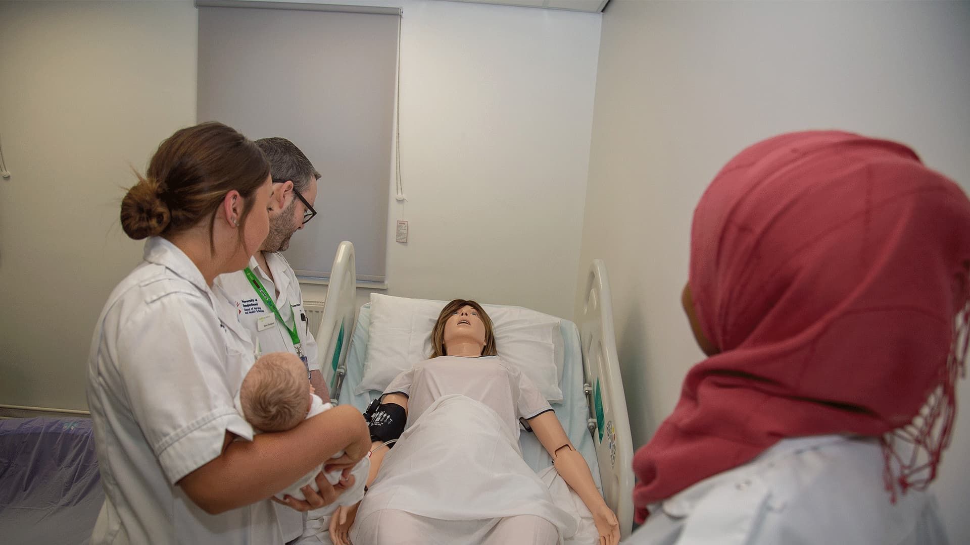 Student midwives and nurses gathered around a manikin, one of them holding the SIM baby