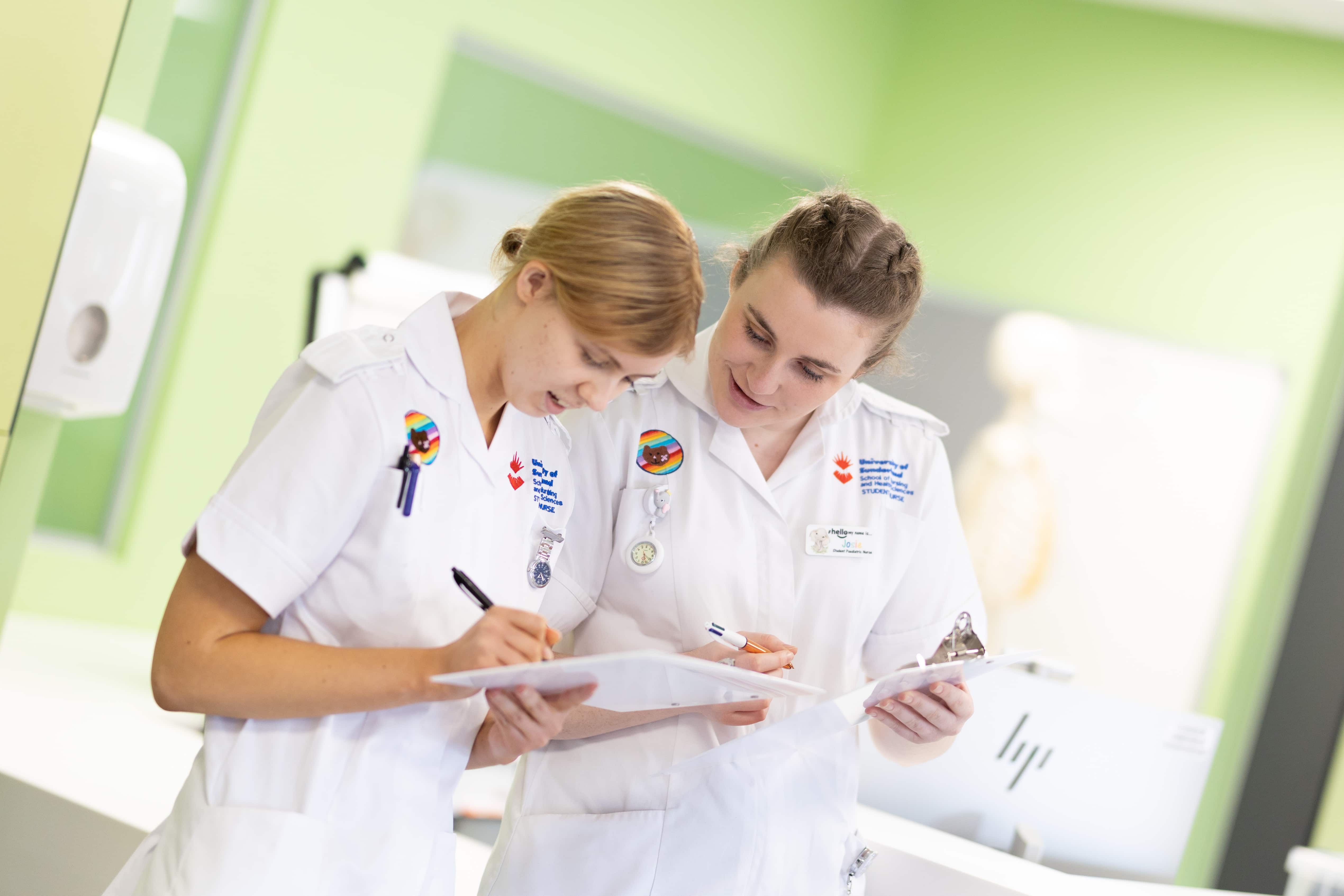 Two student nurses in uniform looking at a clipboard