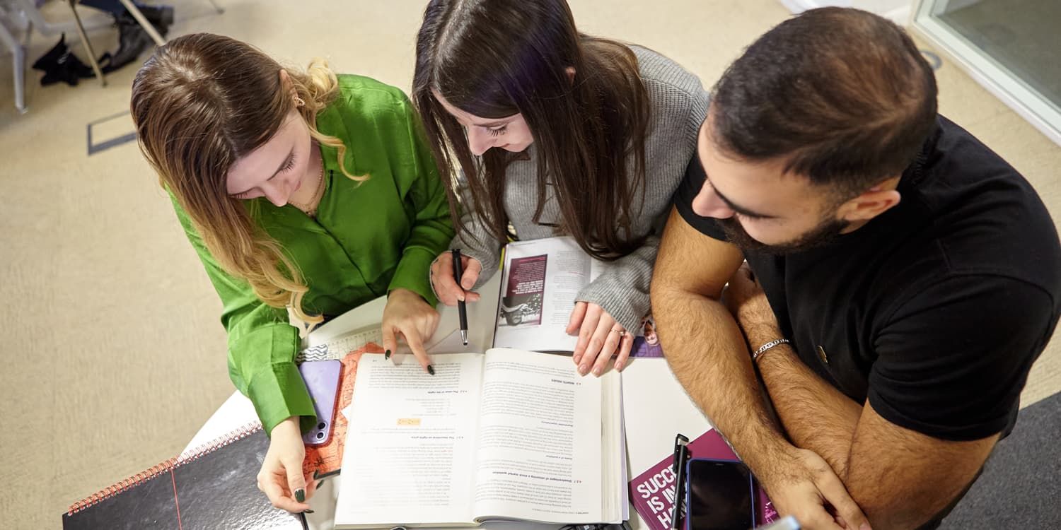 three students studying a textbook together on campus