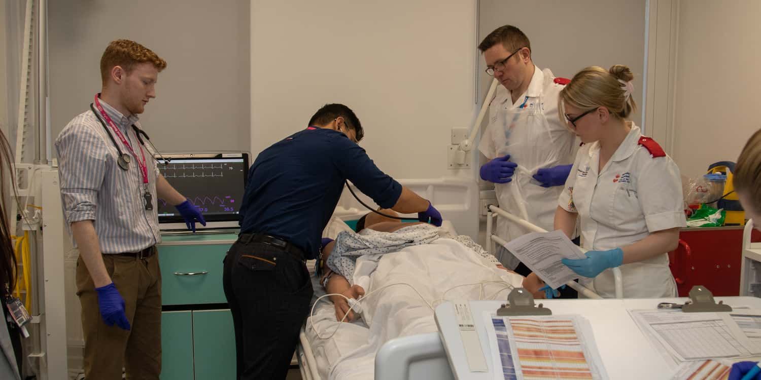 Student nurses and medics working with a simulation manikin in the mock ward