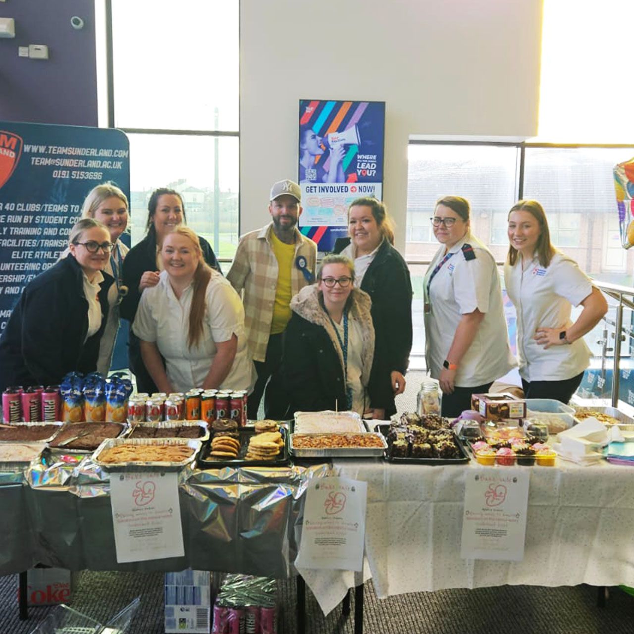 Midwifery students standing behind a table for a bake sale