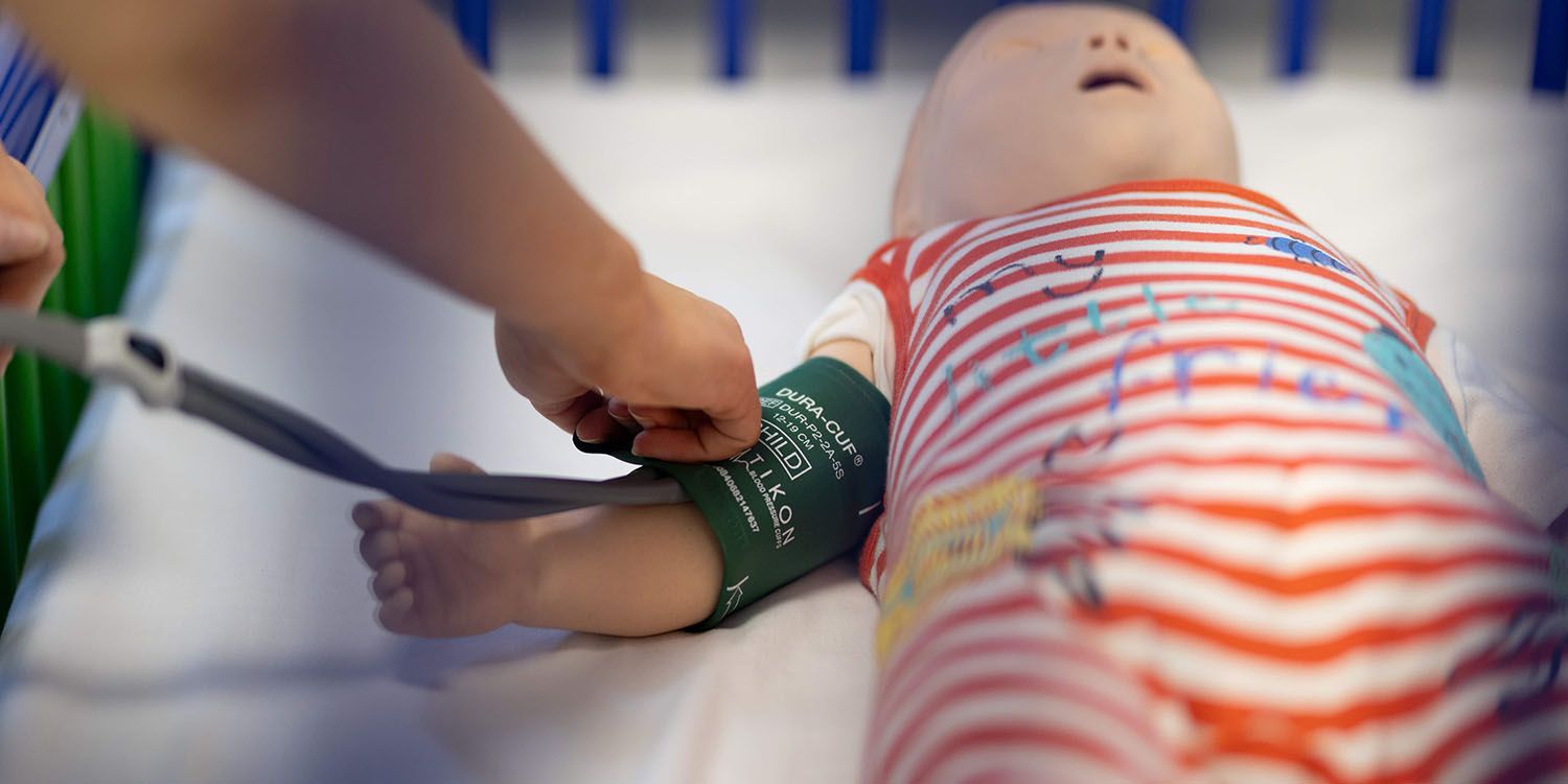 A student nurse using a blood pressure cuff on a manikin infant