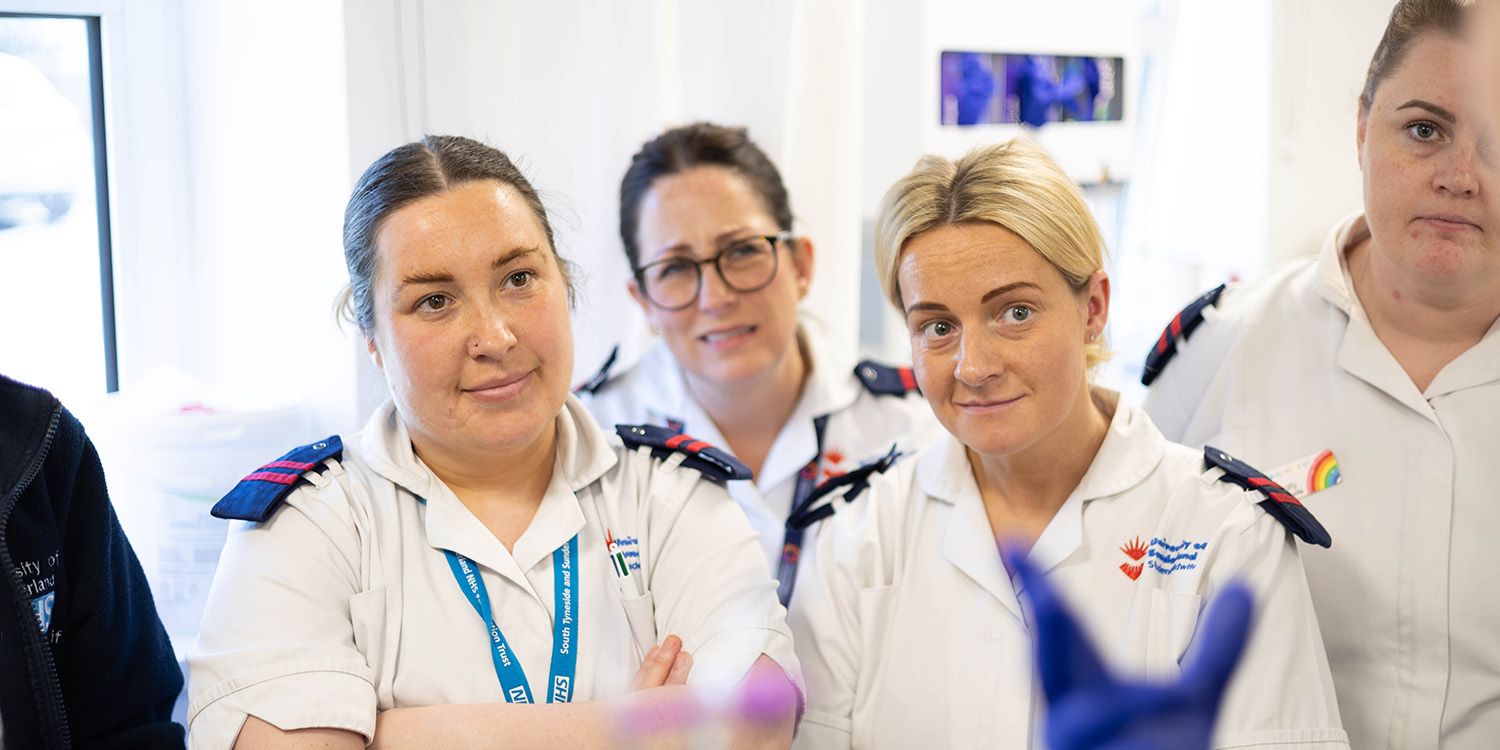 Midwifery students in uniform, listening to someone speak off camera