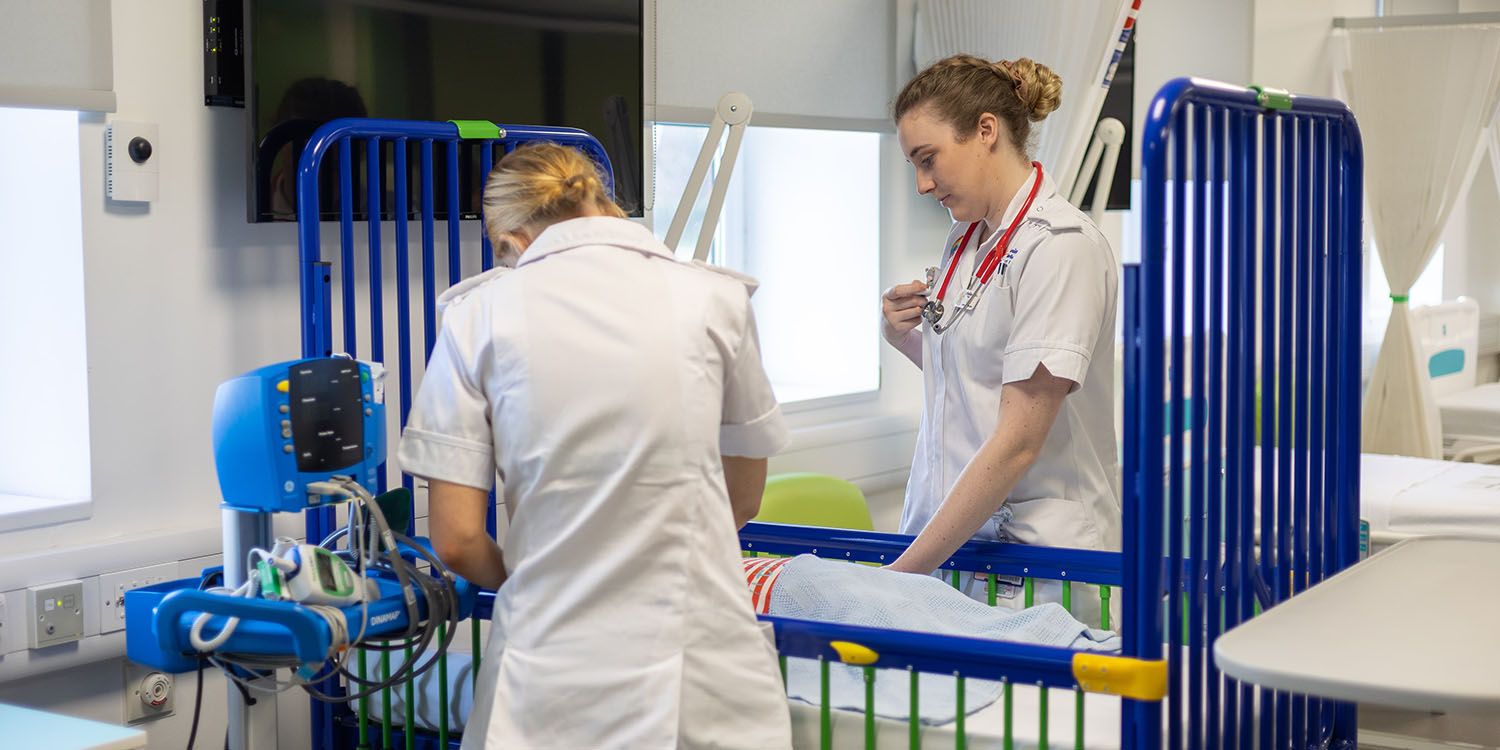 Two nursing students leaning over a crib with a child manikin in the mock ward