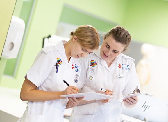 Two student nurses looking down at clipboards in the mock hospital ward