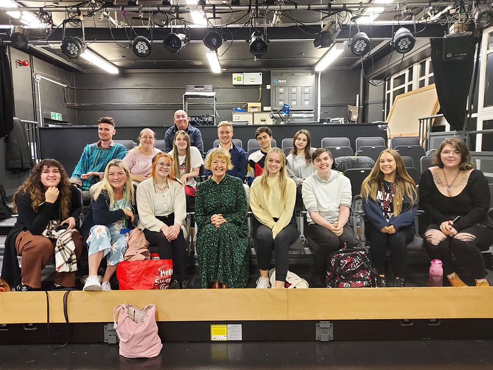 Emmerdale Actor Charlie Hardwick sitting in the middle of a group of Performing Arts students. Everyone is facing the camera and smiling.