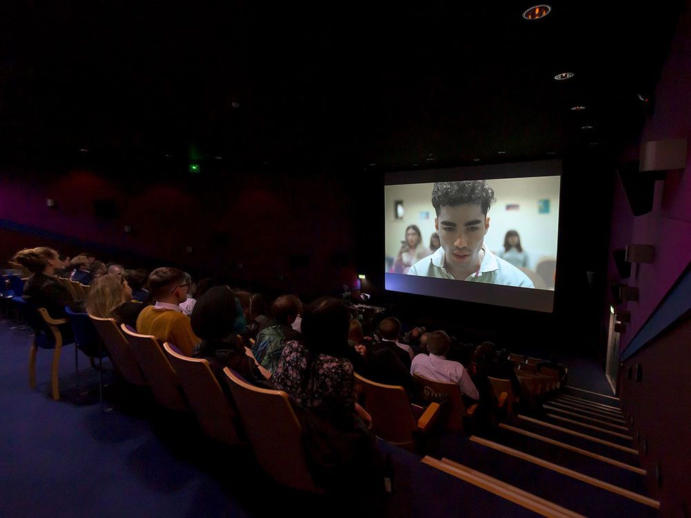 A large group of people sitting in a cinema watching a screening of a film from the Police Project