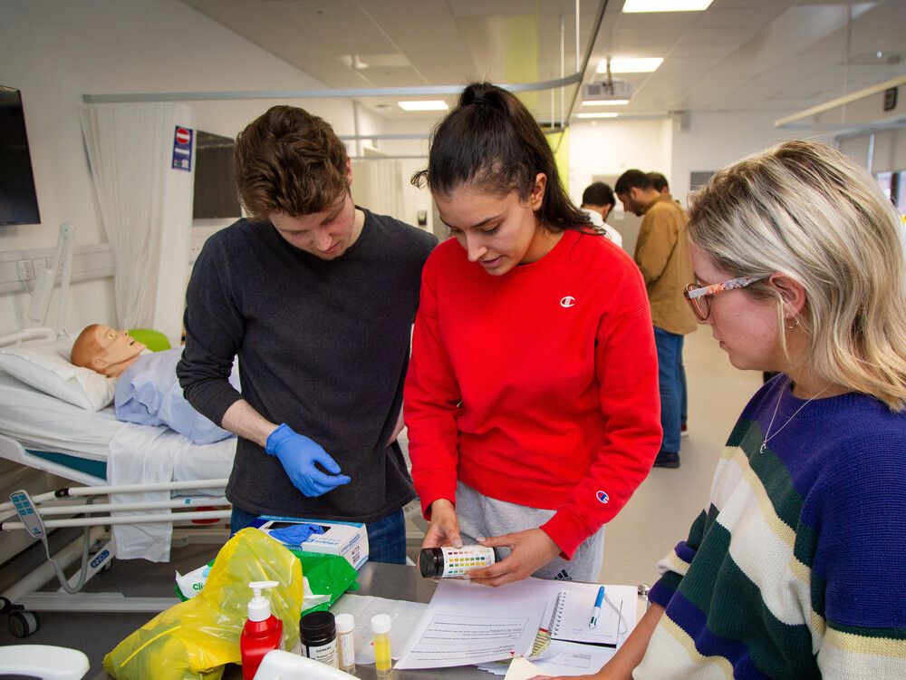 Three pharmacy students working together during a clinical skills session in the mock hospital ward
