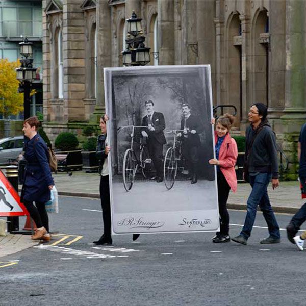 A group of photography students crossing the road in Sunderland city centre carrying a large black and white photograph as part of an exhibition