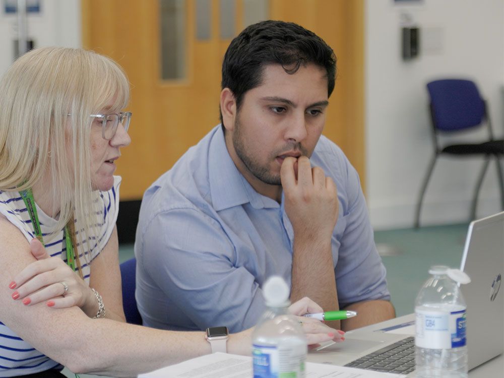 A student showing a member of staff something on their laptop. The staff member looks thoughtful as the student is talking them through what they are looking at