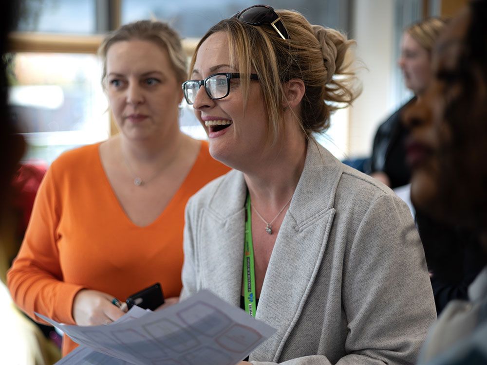 Two members of staff looking at something off camera during a poster presentation. A member of staff in the foreground is smiling widely at what they are looking at