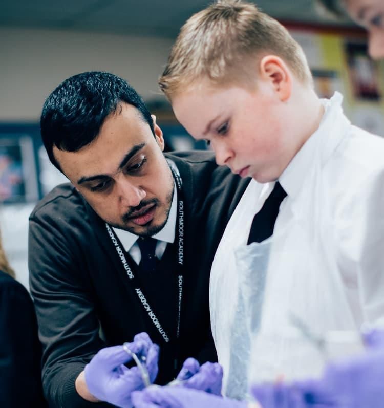 A student helping school children with work who are wearing lab coats and gloves