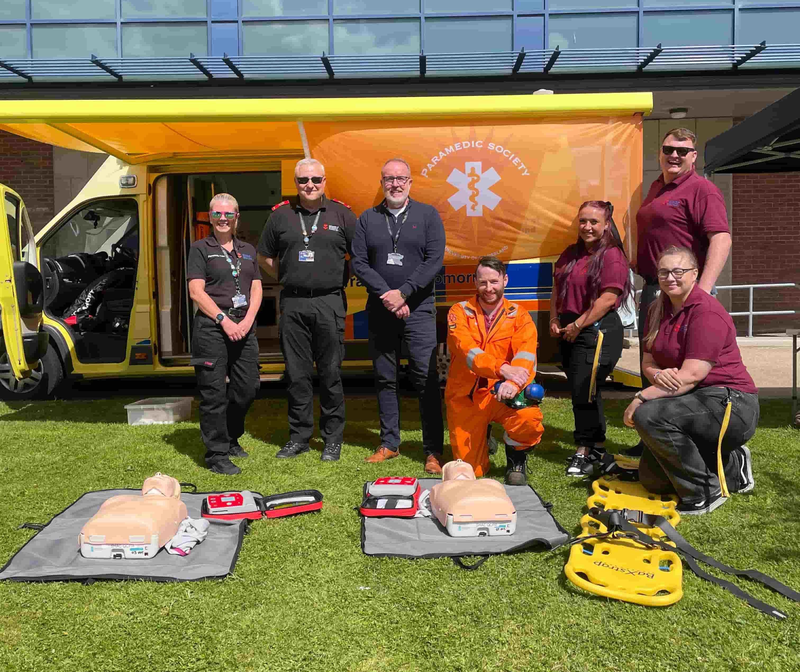 Paramedic lecturers and students standing in front of the simulation ambulance smiling to celebrate International Paramedics Day 2024