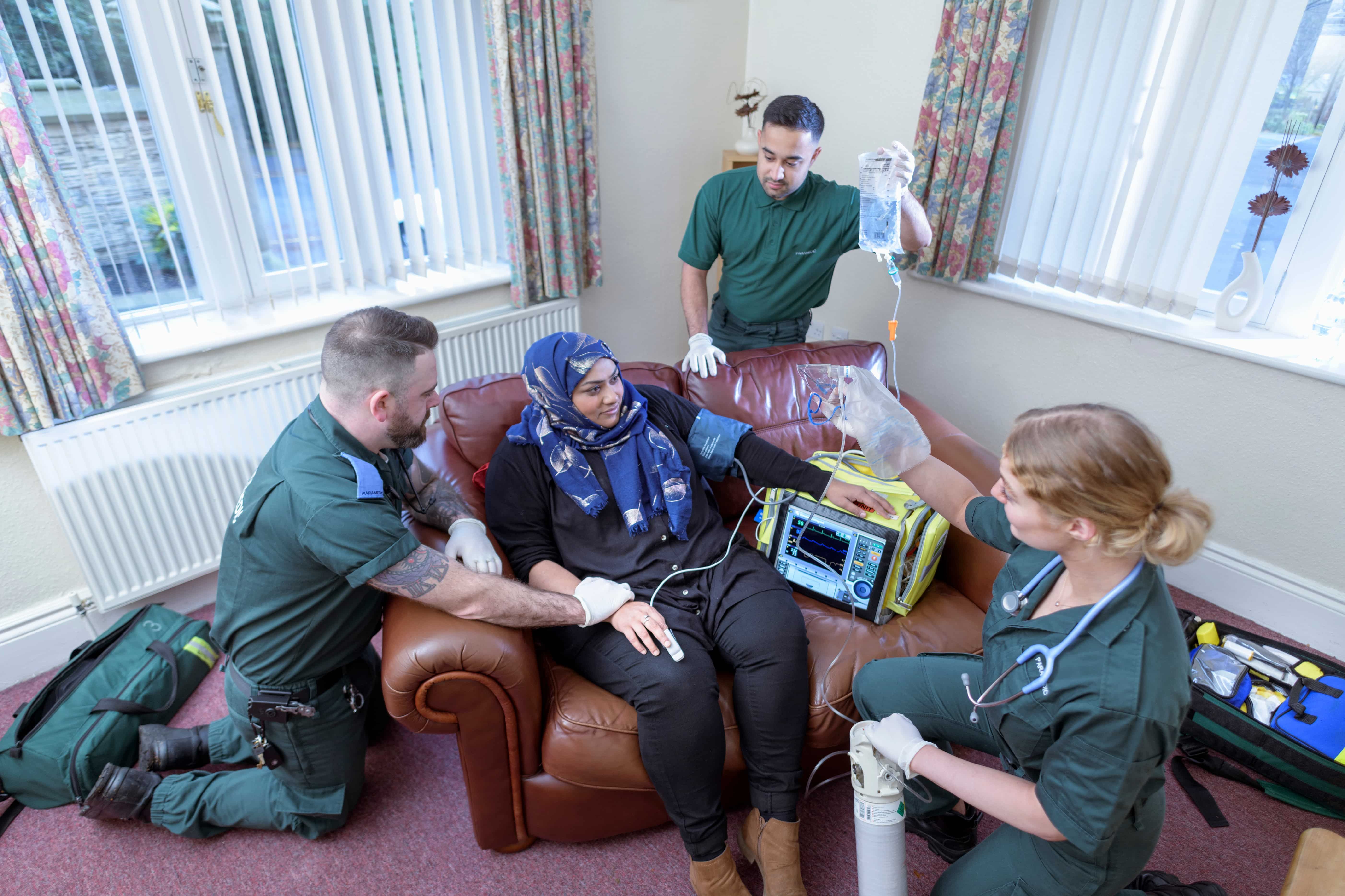Three paramedics attending to a seated patient in their home